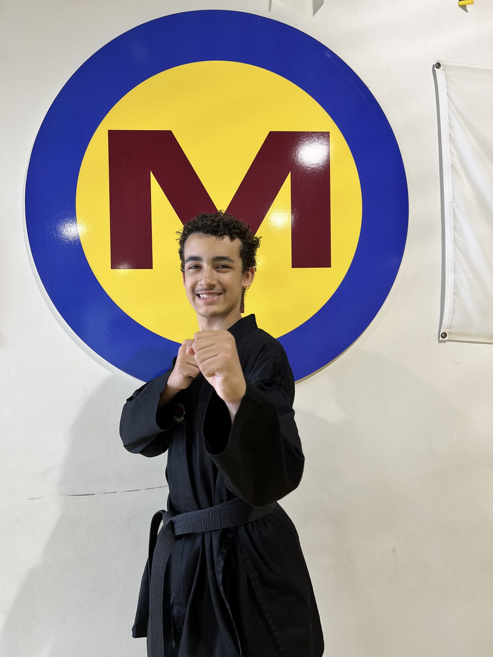 Jarren Searcy in a black uniform, smiling in a fighting stance in front of the studio M