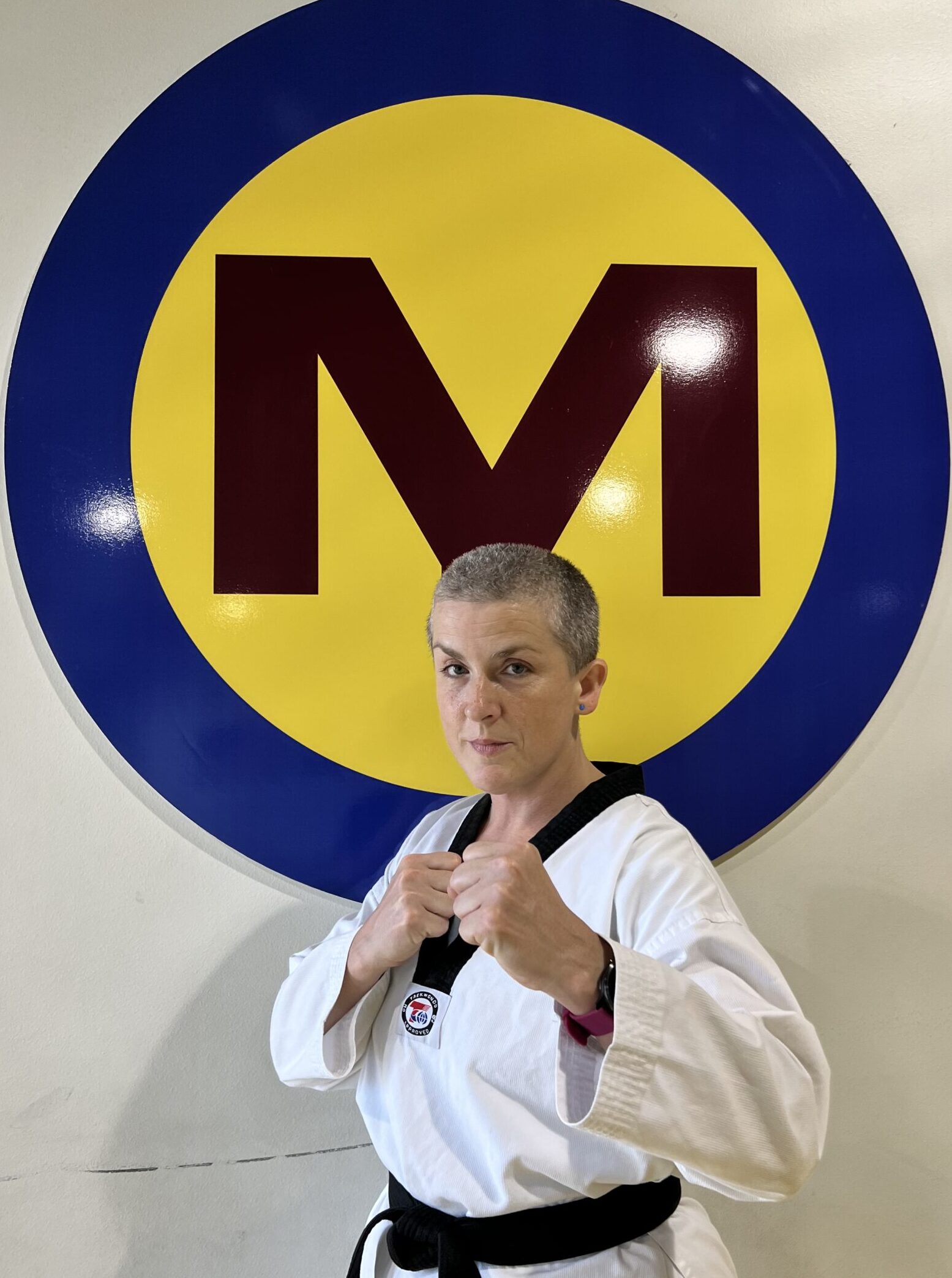 Julie Daniel in a white dobok and black belt, hands up, in front of the studio M